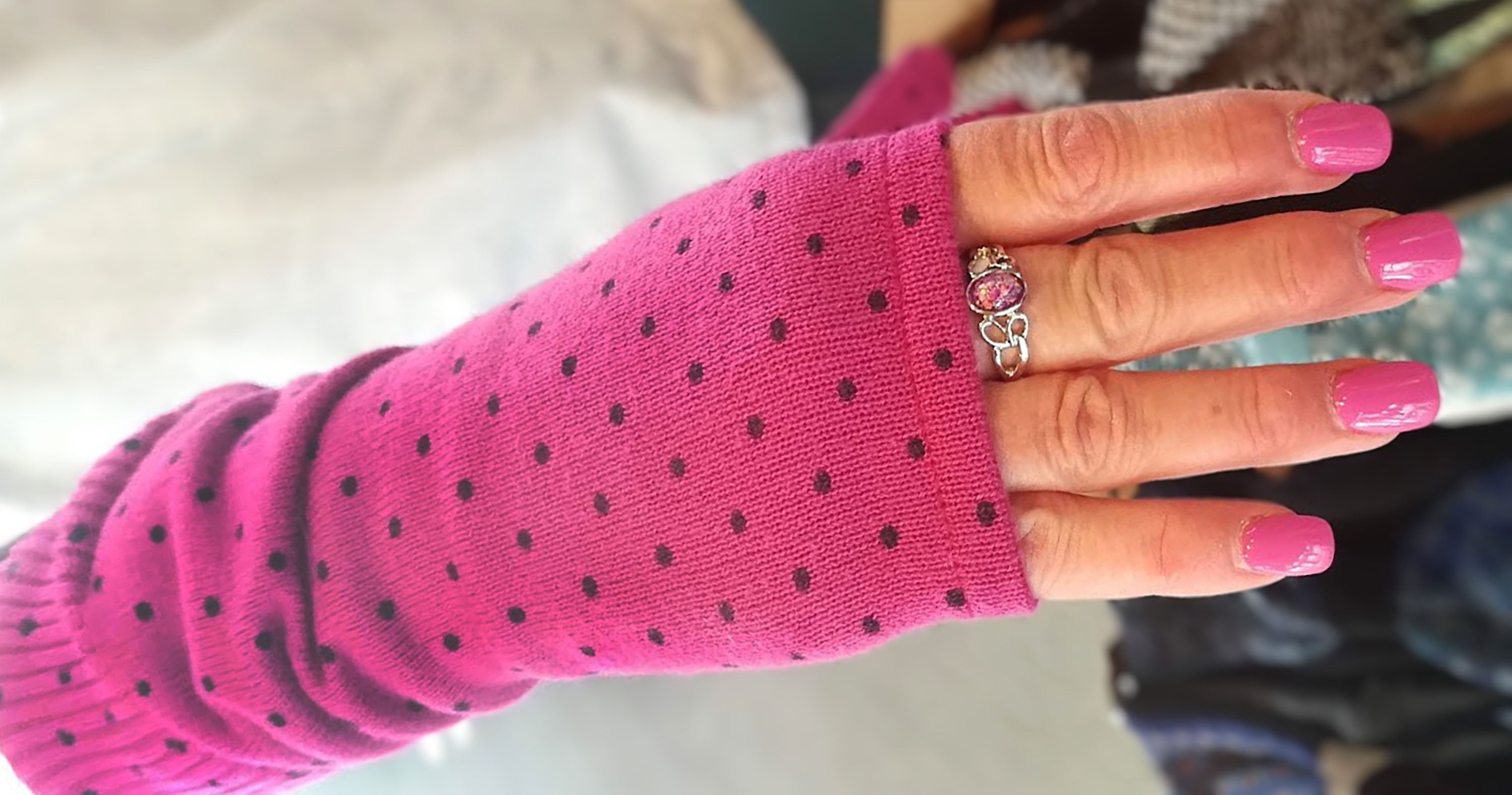 Hand wearing long fingerless Kitten Mittens in pink with black dots