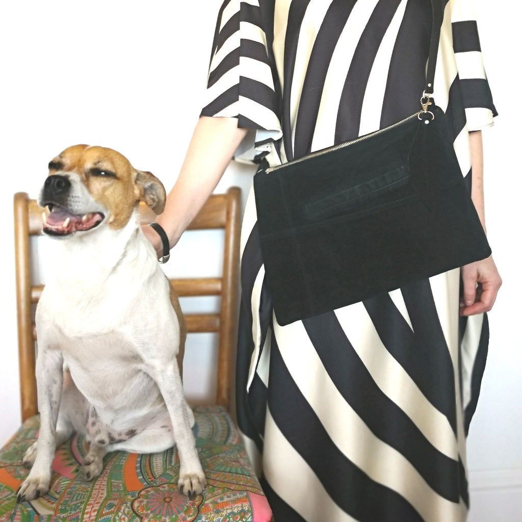 Woman in vintage dress and recycled black suede bag stands next to her dog