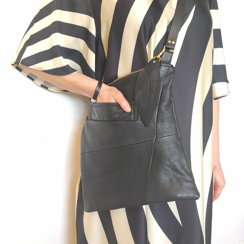 Woman holding recycled black leather crossbody bag with her hand in front pocket